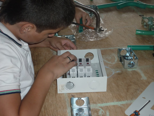 Niño instalando una caja de breakers en un tablero de practicas de instalaciones residenciales