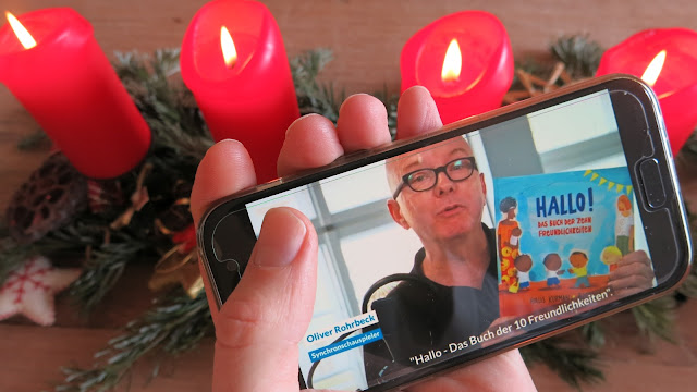 Vor einem Adventskranz ist Oliver Rohrbeck ist auf dem Smartphone zu sehen, wie er die Adventsaktion der UNO-Flüchtlingshilfe unterstützt