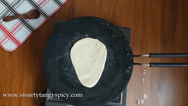 Butter naan dough cooking on a hot tawa (iron griddle) with the wet side facing downward.