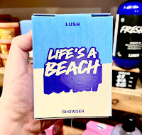A light blue rectangular shaped washing powder style box with lush life’s a beach showder in white font on a bright background