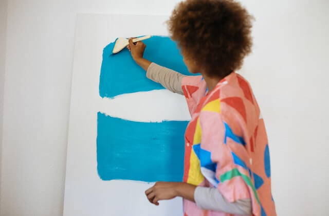 Woman with afro hair painting with blue paint on white canvas
