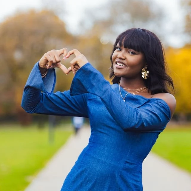 Young woman in blue dress from a heart with her thumbs and forefingers.