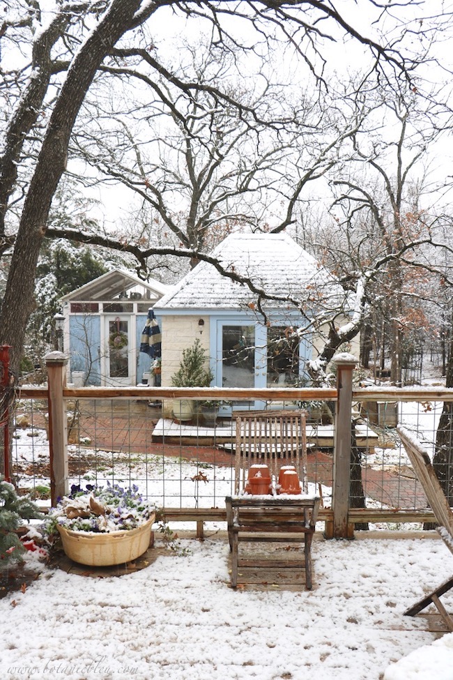 Deck railing made from galvanized wire does not block the view of the beautifulFrench Country garden shed in a snow covered woods