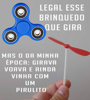 Foto. Na parte superior, um hand spinner azul, um brinquedo giratório composto por um rolamento central com três pontas arredondadas projetadas com variedade de materiais: latão, aço inoxidável, titânio, cobre e plástico. À direita, o texto: Legal esse brinquedo que gira. Abaixo, os dedos: polegar e indicador seguram a extremidade inferior de um pirocóptero, brinquedo composto por um fino palito de plástico branco, na extremidade superior, uma hélice vermelha composta por duas pás. À esquerda o texto: Mas o da minha época: girava voava e ainda vinha com um pirulito.