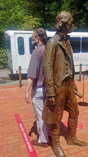 A man stands back-to-back with a metal statue of Thomas Jefferson