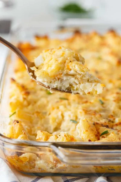 Side view of a spoonful of party potatoes over a casserole dish of party potatoes.