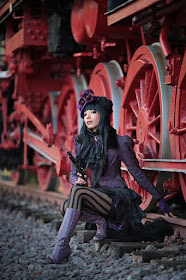 woman wearing steampunk gothic victorian clothes in purple and black. steamgoth style, top hat, skirt, jacket, striped stockings, boots, gun