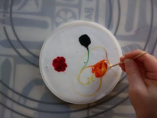 Preschool child moving food coloring around her sun catcher craft with a toothpick