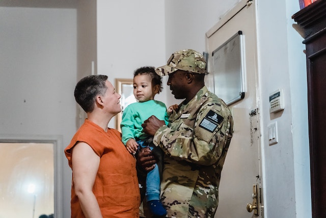 a military man holding a boy and standing near a woman
