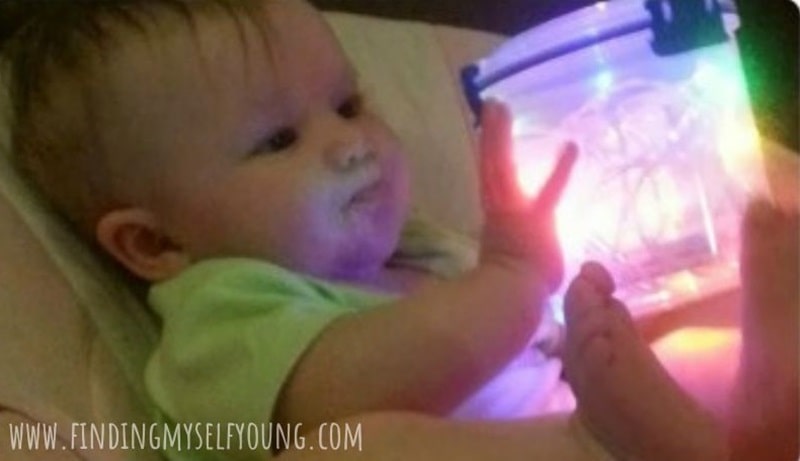 baby holding Christmas lights in a container for sensory play.