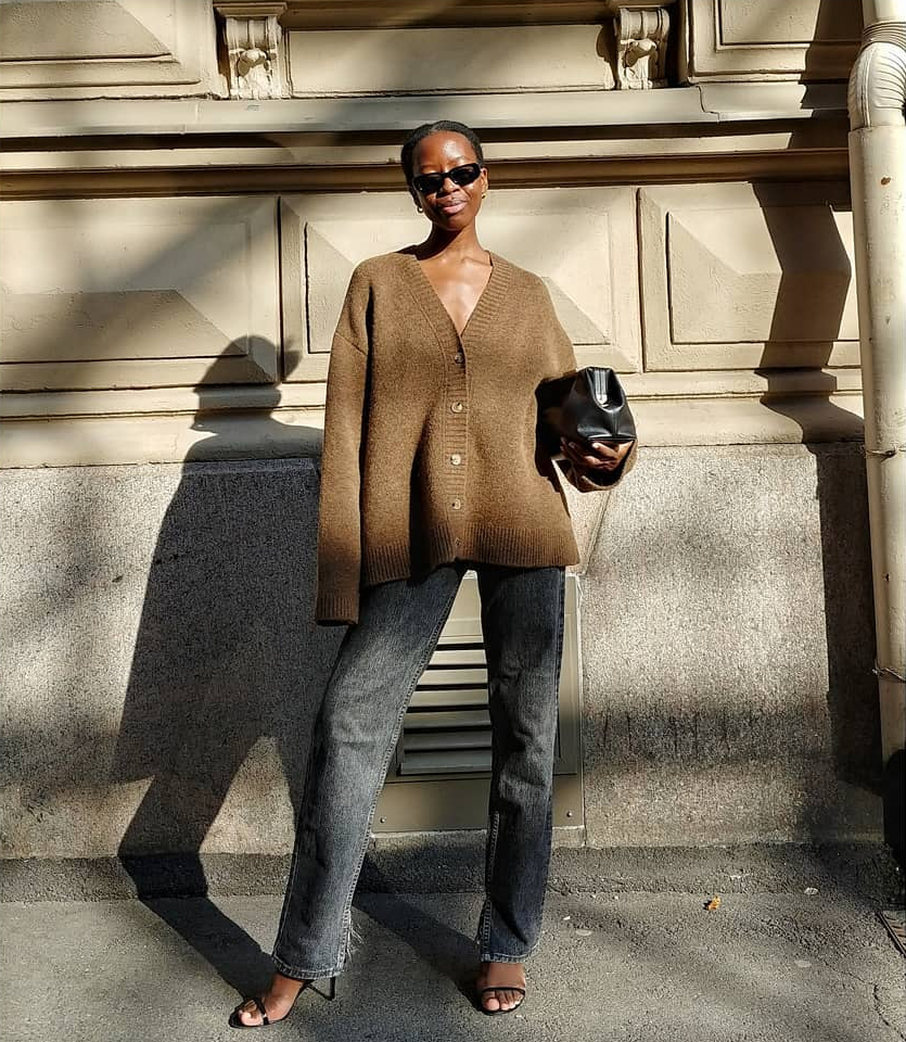 Laid-Back Yet Elevated Fall Outfit Idea — Sylvie Mus in a brown cardigan , black jeans, strappy heeled sandals, '90s-inspired sunglasses, and Demellier London bag
