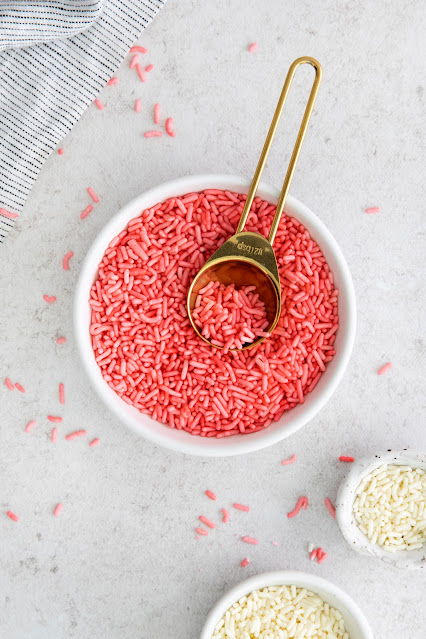 gold spoon sitting in a white bowl with pink sprinkles.