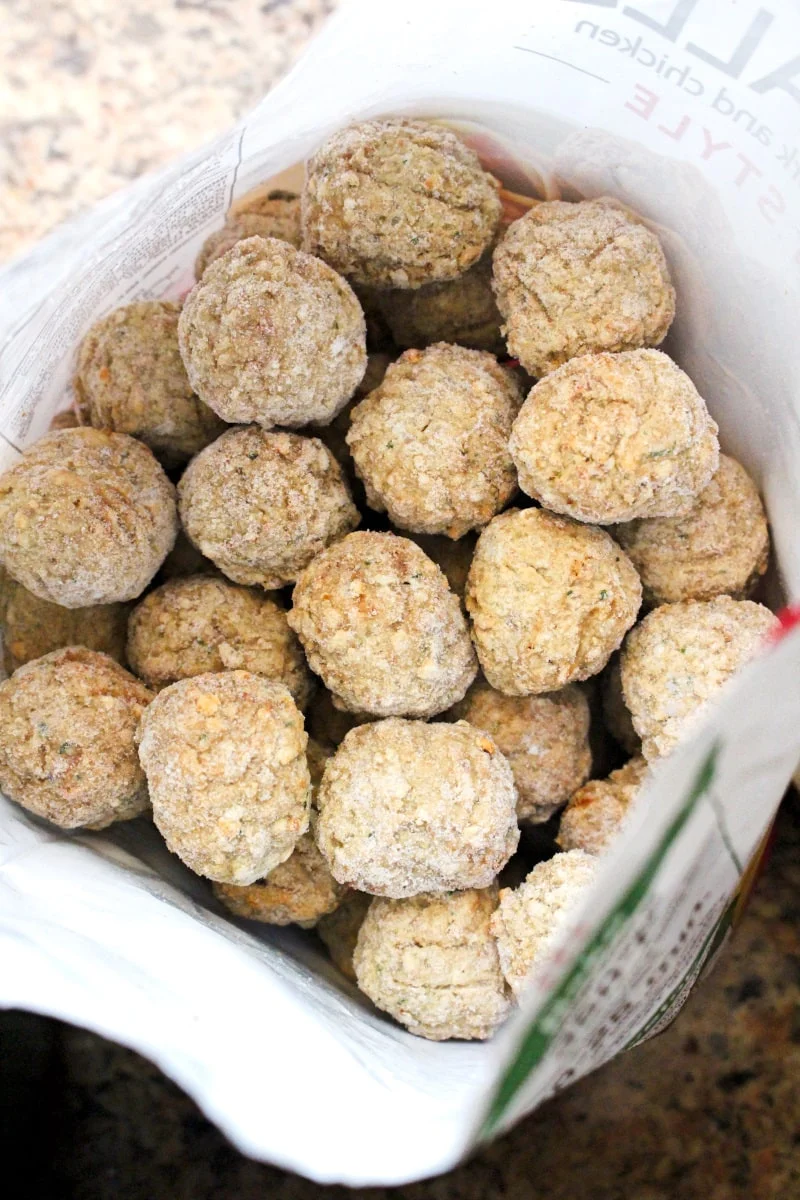 Frozen meatballs in a white bag that has been cut open with scissors.