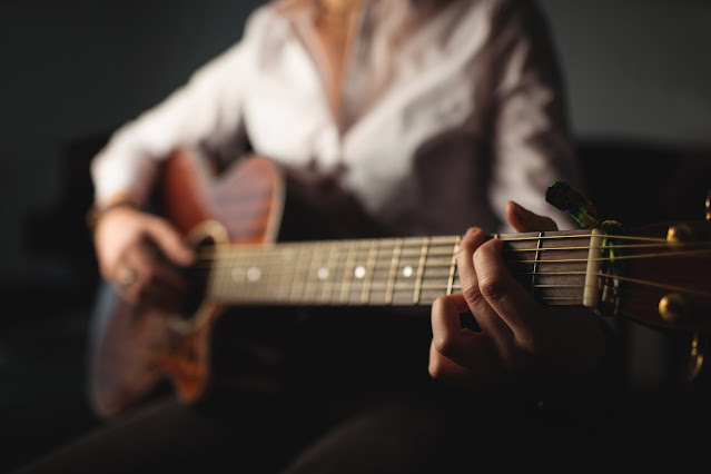 A close up of a woman playing a G chord on the guitar