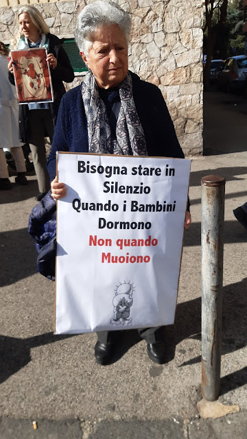 Una donna anziana regge un cartello che recita: bisogna stare in silenzio quando i bambini dormono. Non quando muoiono.