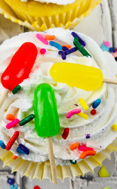 close up of cupcake with candy popsicles on top of frosting.