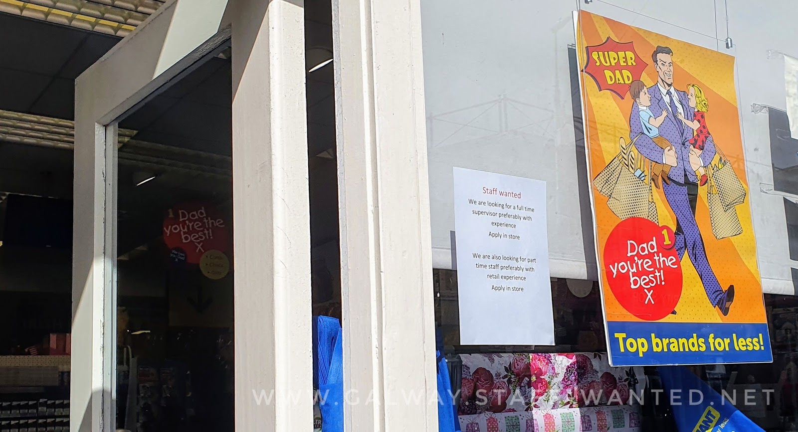 Super dad "dad you're the best" with a cartoon data in a suit and two small children - poster on display beside a staff-wanted sign in Galway city