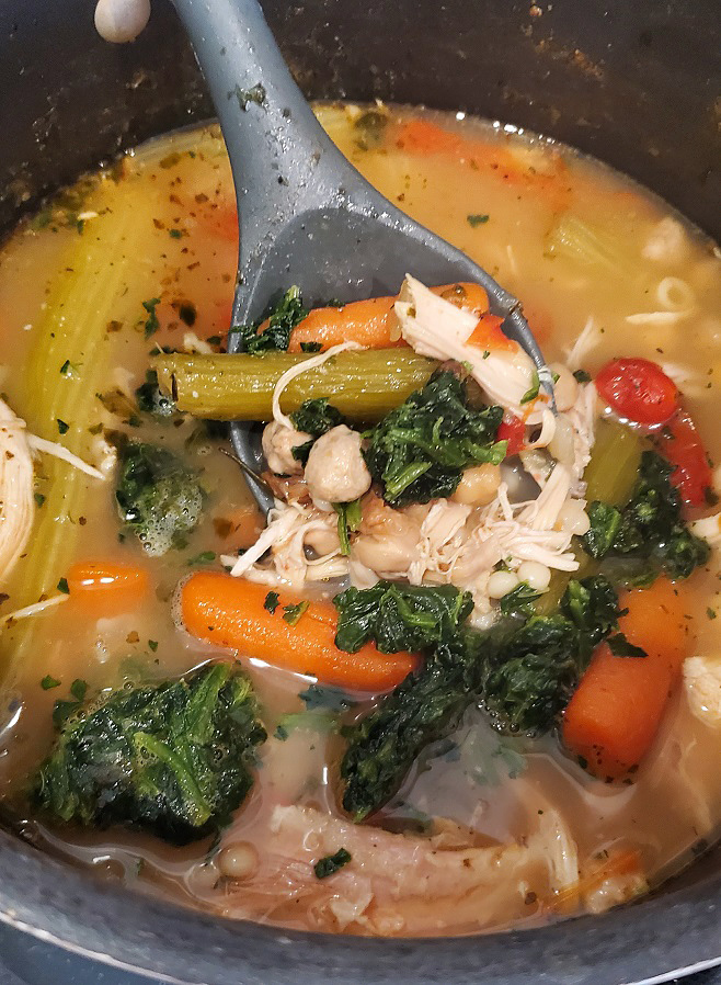 a pot of chicken soup with spinach and vegetables