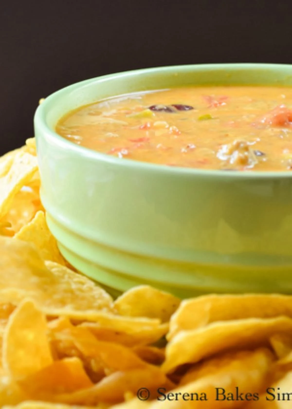 A side shot of Chili Con Queso Dip in a light green bowl with tortilla chips around the edge.