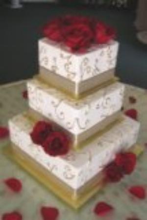 The cake is iced in ivory buttercream with hand painted gold scroll work and