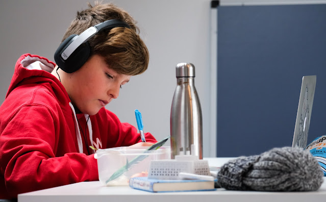 young boy wearing headphone leaning over to write