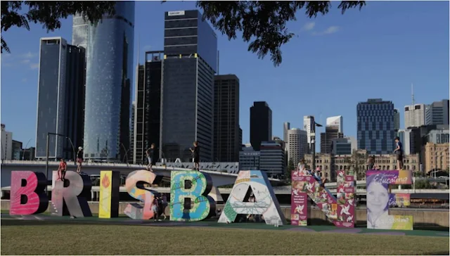 Imagem de Brisbane, com prédios ao fundo e letras formando o nome da cidade sobre um gramado