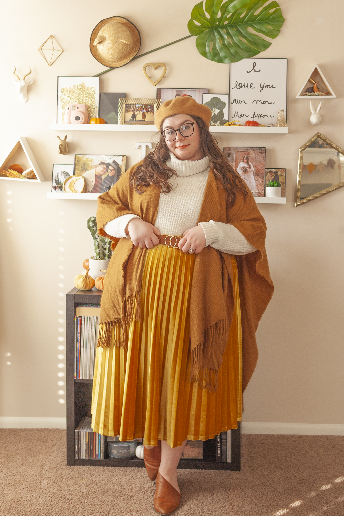 An outfit consisting of a tan brown shawl over a white cream chenille turtleneck sweater tucked into a velvet yellow pleated midi skirt and cognac brown d'orsay flats.