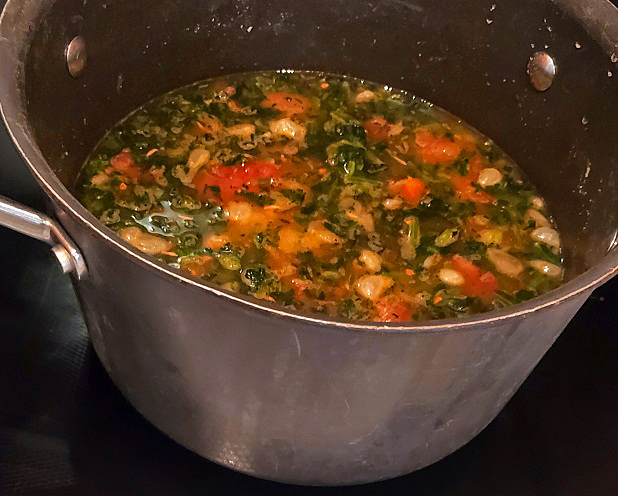 spinach with tomatoes and white beans simmering in a soup pot