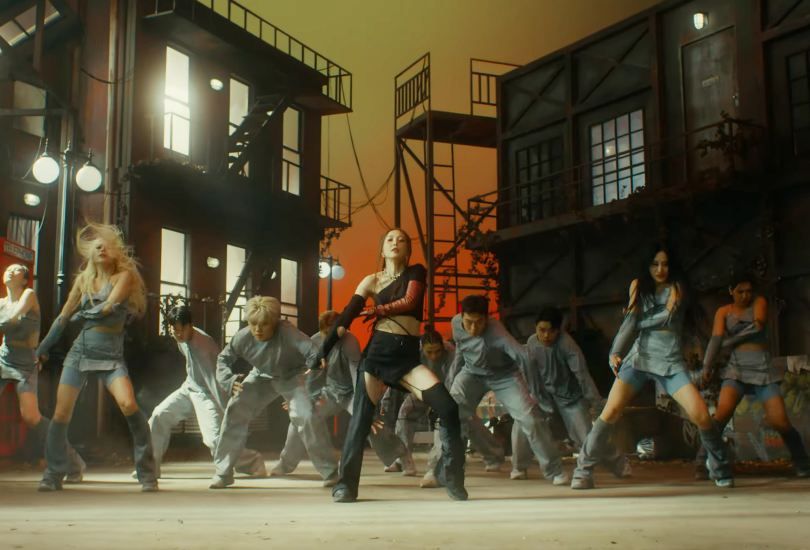 BoA dancing with her dancers, on a soundstage set built to look like a street alleyway at sunset. BoA is wearing black. Her dancers are all wearing light stonewashed denim.