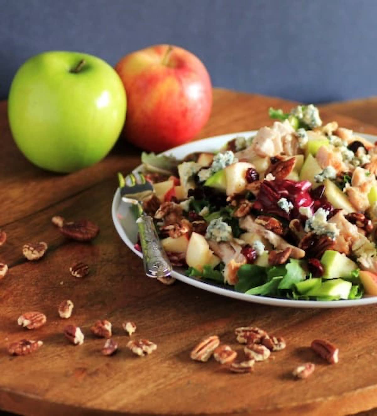 A side shot of Copycat Wendy's Apple Pecan Chicken Salad on a wooden cutting board with pecans around the edge.