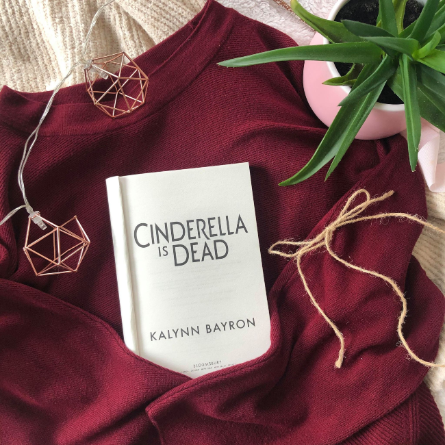 Title page of 'Cinderella is Dead' on a burgundy jumper with a string of fairy lights around it