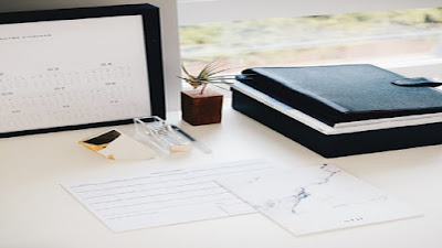 Small business work station with a computer screen, work sheets, a black brief case and sundry small work tools.