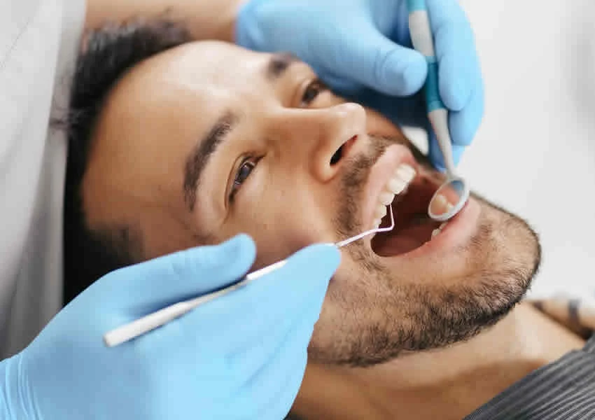 Imagem mostra um homem com a boca aberta na cadeira do dentista sendo examinado.