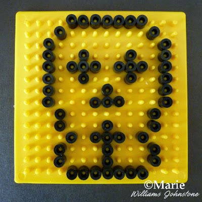 Yellow board with black Perlers on the pegs making a skull face shape