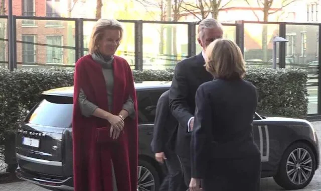 Queen Mathilde wears a black and white checked dress, with a wine-red cape coat by Natan. Diamond parrots brooch