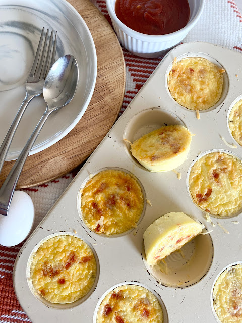 Overhead shot of pizza egg bites in a muffin tin with a plate and silverware by it.