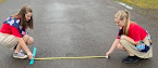 Two young women using a measuring tape to determine the distance of a cotton ball from the starting line.