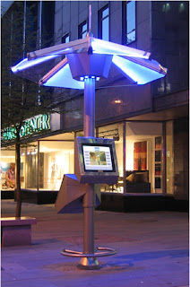 From concept to street deployment the PUBLIC DATAWEB UMBRELLA kiosk operating in the city centre in Aberdeen Scotland. The picture shows the kiosk at night with its illuminated top Umbrella highlighting the area in a pool of blue light. © PUBLIC DATAWEB
