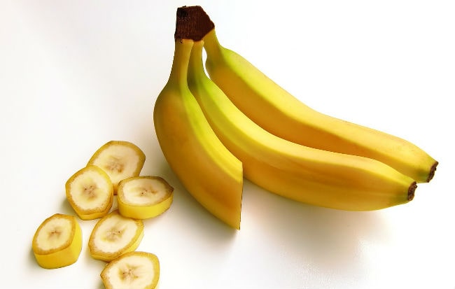 Banane intere e a pezzi su fondo bianco