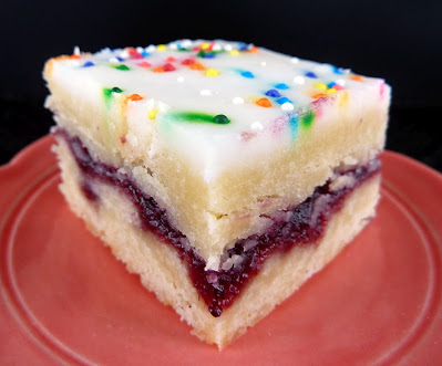 Pop Tart Inspired Shortbread Bars: two layers of shortbread dough sandwiched with preserves, topped with powdered sugar icing and colorful sprinkles. Photographed on an orange plate.