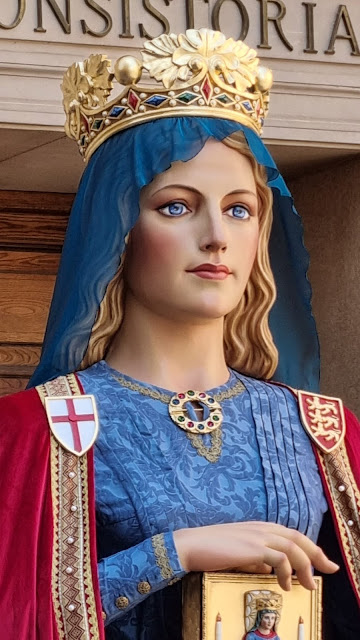 Foto de medio cuerpo de la giganta Berenguela. Es rubia, luce corona real, tocada por manto azul a juego con el vestido. En la capa carmesí, heraldica del reino de Navarra.velo zu manto az y Luce corona