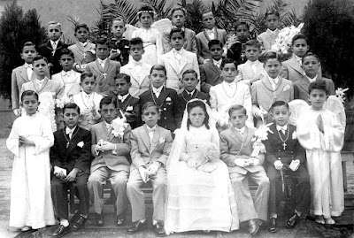 Año 1948: Niños de un Colegio de hijos de obreros ferroviarios, de padres mayoritariamente “rojos” exiliados en Lérida, el día de su Primea Comunión. Se les ve “torturados” por la “dictadura franquista”, mal vestidos y famélicos (soy el 4º sentado empezando por la izquierda con cara de “mala uva”, al lado de la niña) 