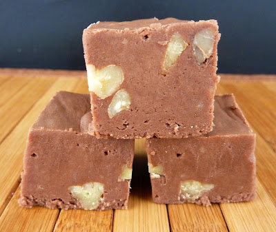Three pieces of classic chocolate pecan fudge, photographed on a blonde wood mat.