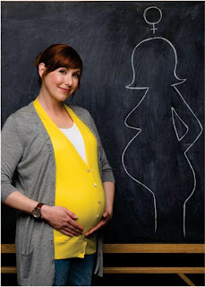 A pregnant teacher in front of a blackboard with a drawing of a pregnant lady