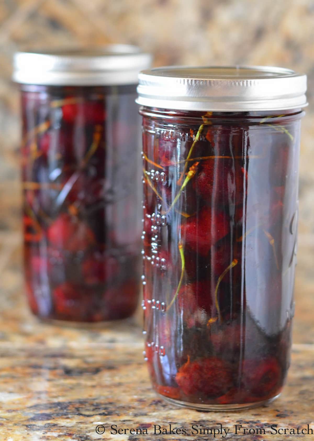 Whiskey Cherries in a tall masons jar with a lid on a granite counter top.