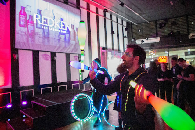 Artistas com malabares de luzes circulando entre convidados do evento da empresa Redken em SP.