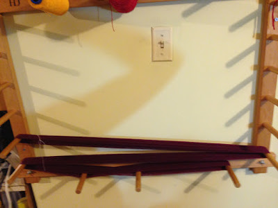 A short maroon warp on the lowest three rows of pegs on a wooden warping board.