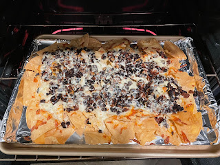 Chips, cheese, beans, and soy chorizo on a foil lined pan in the oven.