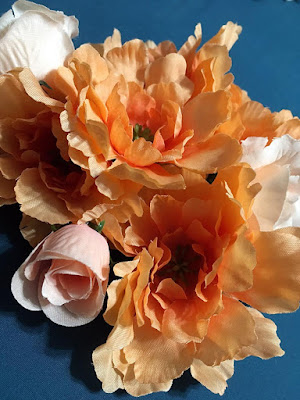 A cluster of ruffly peach fake flowers and pale-pink fake roses on a teal background.