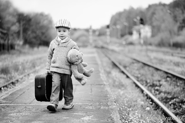 Mały chłopiec z misiem i walizką idzie po peronie stacji PKP przy torach wraca z podróży